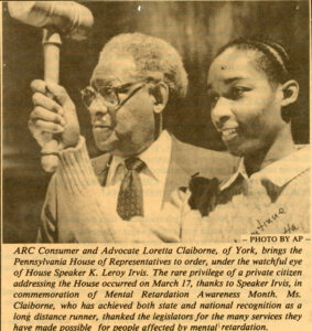 Old blank and white photograph of Loretta Claiborne and former PA House of Representative speaker K. Leroy Irvis. Loretta is holding up a gavel. "ARC Consumer and Advocate Loretta Claiborne, of York, brings the Pennsylvania House of Representatives to order, under the watchful eye of House Speaker K. Leroy Irvis. The rare privilege of a private citizen addressing the House occurred on March 17, thanks to Speaker Irvis, in commemoration of Mental Retardation Awareness Month. Ms. Claiborne, who has achieved both state and national recognition as a long distance runner, thanked the legislators for the many services they have made possible for people affected by mental retardation.